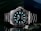 A luxury wristwatch with a luminous dial and markers, featuring a stainless steel bracelet and a rotating bezel. The watch face is adorned with the brand logo, offering a sleek and polished appearance against a dark background.