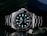A luxury wristwatch with a luminous dial and markers, featuring a stainless steel bracelet and a rotating bezel. The watch face is adorned with the brand logo, offering a sleek and polished appearance against a dark background.