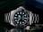 A luxury wristwatch with a luminous dial and markers, featuring a stainless steel bracelet and a rotating bezel. The watch face is adorned with the brand logo, offering a sleek and polished appearance against a dark background.