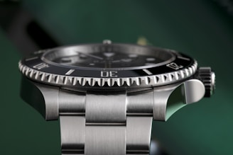 A close-up view of a luxury watch with a stainless steel band and a rotating bezel, showcasing the craftsmanship and detailed design of its structure. The watch face is partially visible with hour markers and hands.