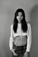 Monochrome shot of a model wearing a charcoal hoodie, standing against a concrete wall with shadows