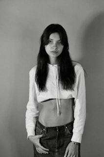 A minimalist, monochrome photo of a young person wearing stylish, well-fitted fenr clothing, standing against a plain background.