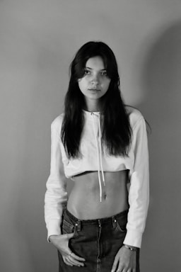 A minimalist, monochrome photo of a young person wearing stylish, well-fitted fenr clothing, standing against a plain background.