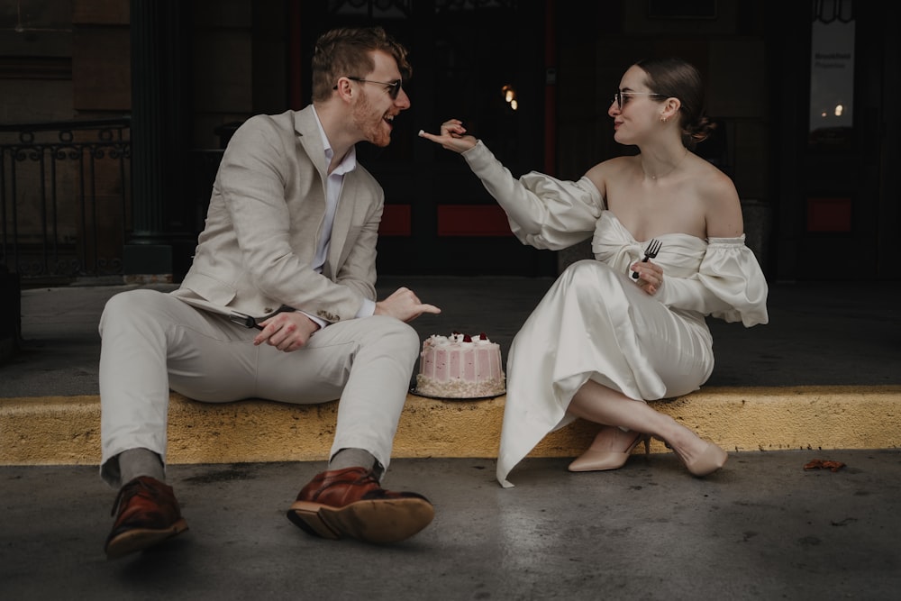 a man and a woman sitting on a ledge with a cake