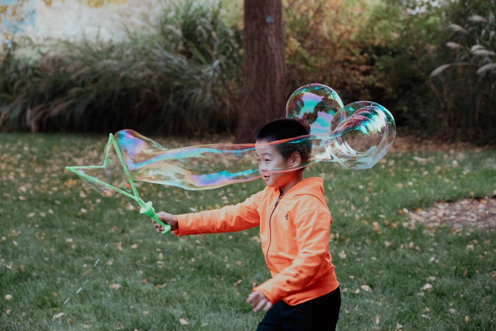 a boy in an orange jacket is playing with bubbles