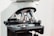A close-up of a microscope, focusing on the objective lenses. The lenses are metallic with engraved magnification details, surrounded by a black rotating disk. The microscope's stage is visible beneath the lenses with a holder mechanism for slides.