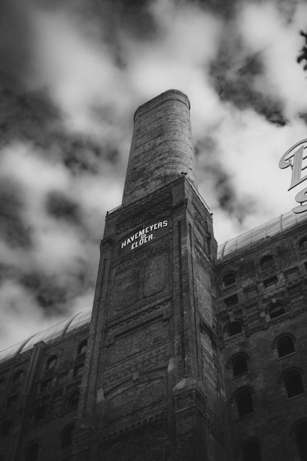 A tall, industrial building with a large smokestack towers against a cloudy sky. The words 'Havemeyers & Elder' are visible on the building facade, which is adorned with intricate brickwork and arched windows.