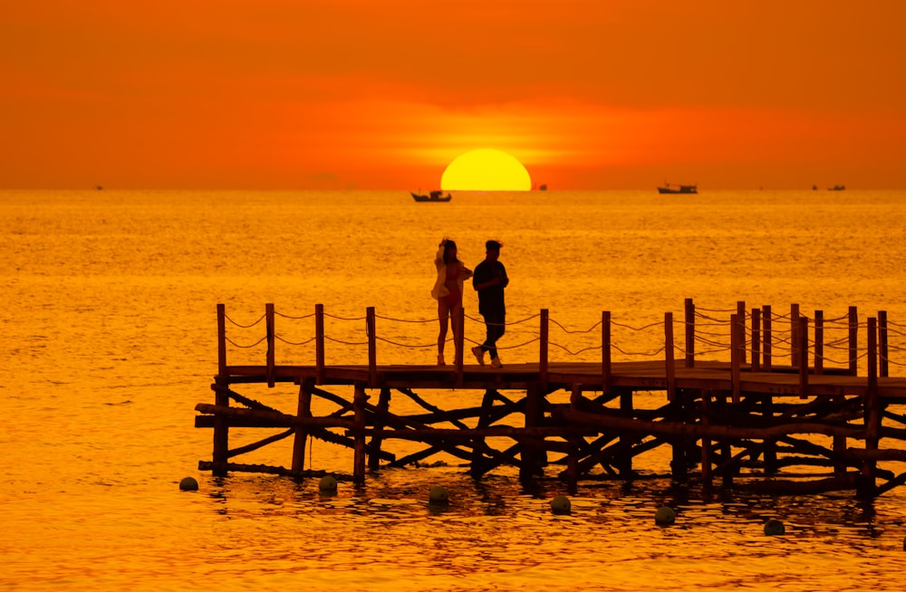 a couple of people standing on top of a wooden pier