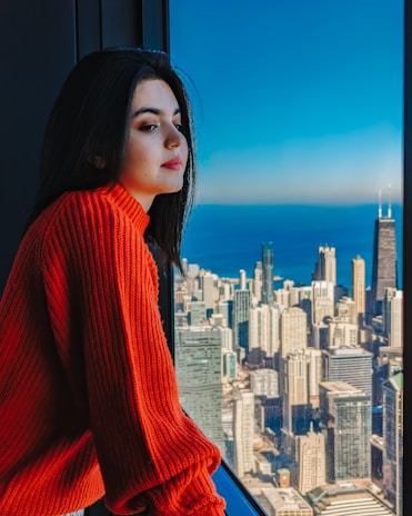 A model wearing a luxurious cashmere sweater in a rich autumn tone, standing by a city window.