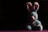 A plush blue bunny with pink inner ears and a pink nose is positioned against a dark background. The bunny is wearing a sheer ribbon tied around its neck and is sitting in a spotlight that highlights its fluffy texture, creating a strong contrast with the surrounding shadows.