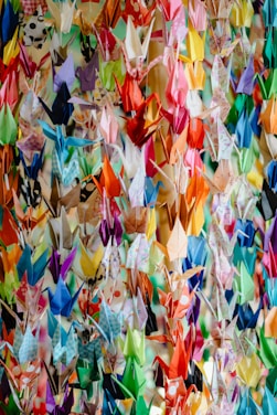A colorful assortment of origami paper sheets neatly stacked with a few folded paper cranes displayed.
