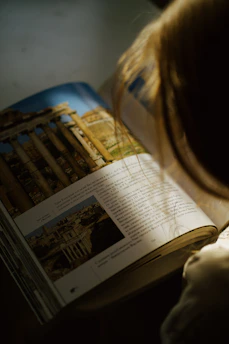 Close-up image of a child reading a book with a hopeful expression in a sunlit room.