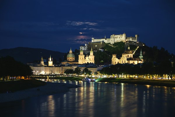 A castle is lit up at night by the water — Salzburg, Austria