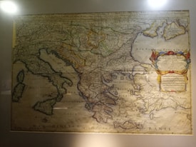 An antique map featuring various regions including parts of Europe and the Mediterranean, intricately detailed with geographical features and labeled in a classical script. A decorative cartouche on the right side contains a colorful emblem and text.