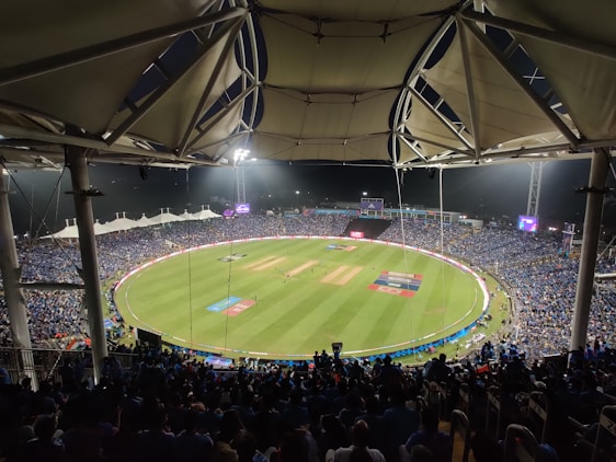 A lively cricket stadium filled with cheering fans under bright floodlights during an intense match.