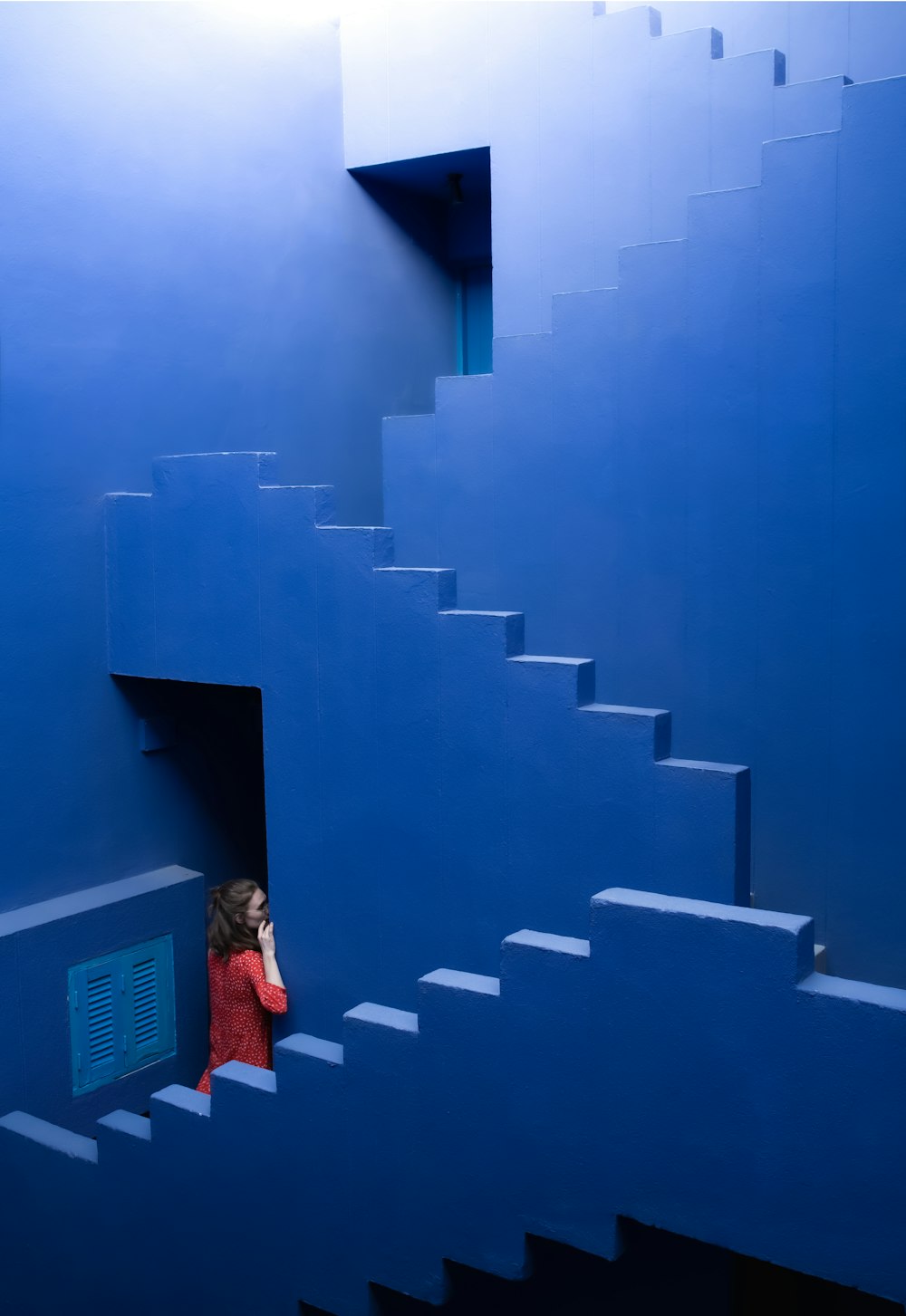 a woman in a red coat is standing on a blue staircase