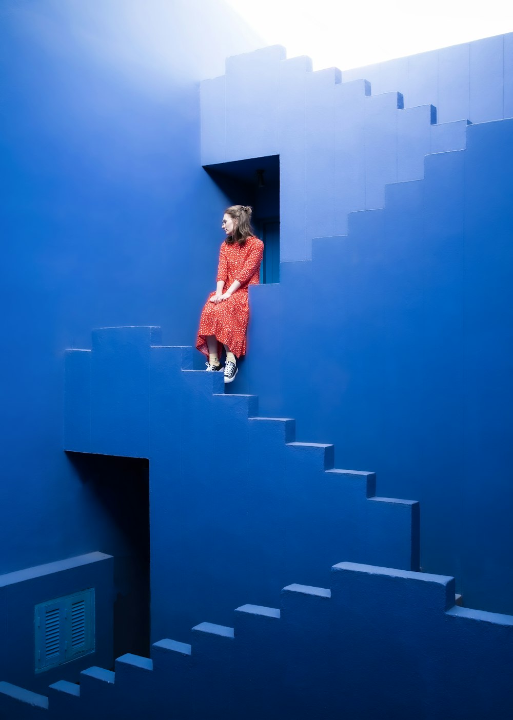 Une femme vêtue d’une robe rouge est assise sur un escalier bleu
