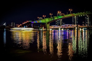 A bustling cityscape at night with colorful lights reflecting on a river