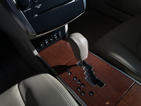 A car interior featuring a gear shift panel with a wood finish and leather upholstery. The gear shift lever is positioned centrally, surrounded by buttons and an automatic gear shift slot. The panel displays options for gear selection.
