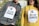 Two individuals are wearing placards with the message 'STOP RACISM' printed on them, accompanied by a handprint graphic. The person on the left is wearing a gray hoodie, while the person on the right is dressed in a yellow hoodie. The placards are attached with red tape. Graffiti and trees are visible in the background.