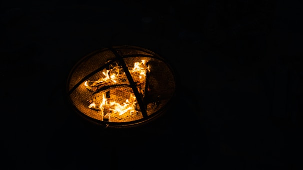 A handcrafted metal fire pit with bright orange flames flickering against a dark wooded backdrop.