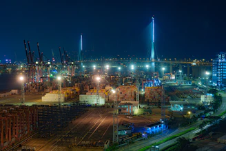 An aerial view of a bustling port with cranes and containers illuminated under night lights