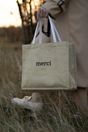 Hand holding a beige personalized tote bag with subtle branding outdoors