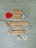 Wooden Scrabble tiles spell out the phrase 'What are you grateful for today?' on a light wooden surface. Two decorative curling ribbons, one gold and one silver, are positioned around the text. A small red heart and a white heart-shaped paper with written text are included in the scene.