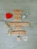 Wooden Scrabble tiles spell out the phrase 'What are you grateful for today?' on a light wooden surface. Two decorative curling ribbons, one gold and one silver, are positioned around the text. A small red heart and a white heart-shaped paper with written text are included in the scene.