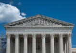 The image presents the facade of a neoclassical building with grand columns and intricate sculptures atop the pediment. The structure is made of stone, and the frieze bears the inscription 'EQUAL JUSTICE UNDER LAW.'