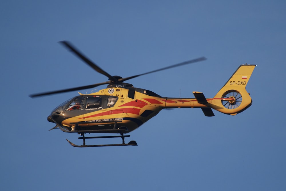 a yellow and red helicopter flying through a blue sky