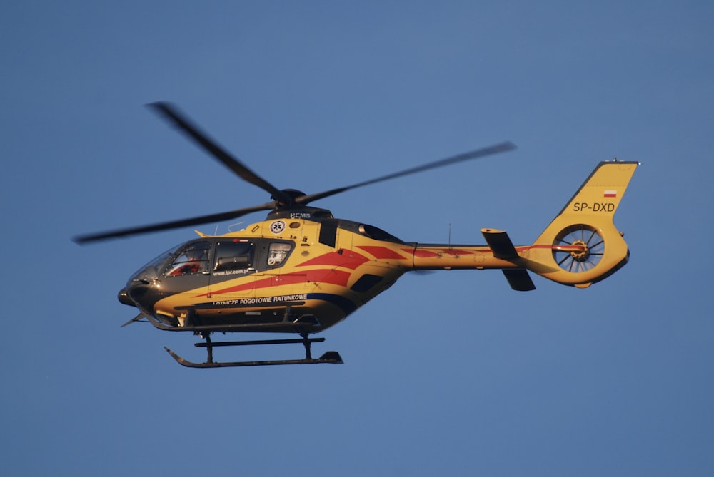 un helicóptero amarillo y rojo volando a través de un cielo azul