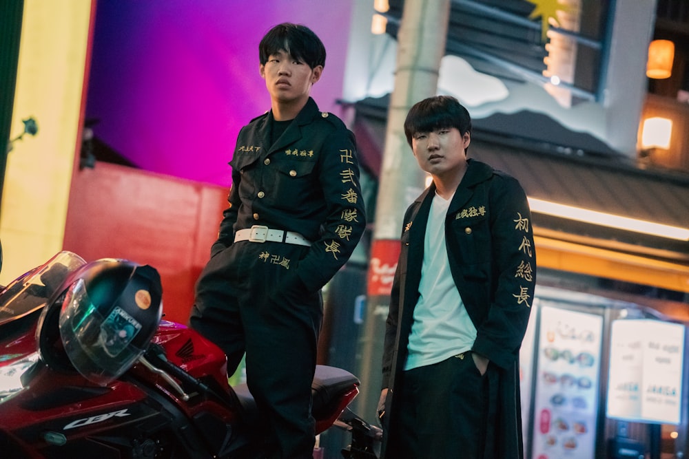 two young men standing next to a motorcycle