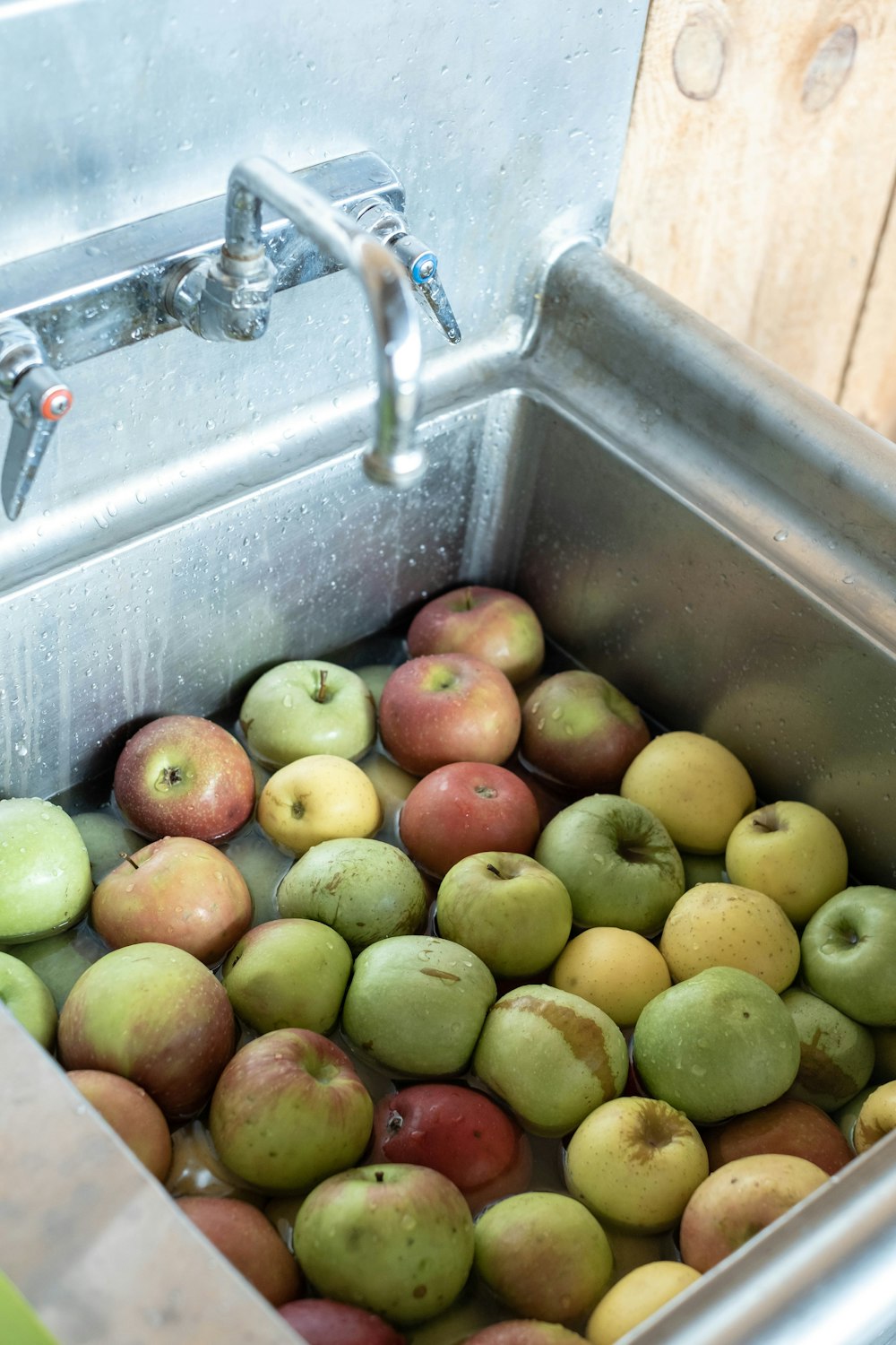 a metal sink filled with lots of green and red apples