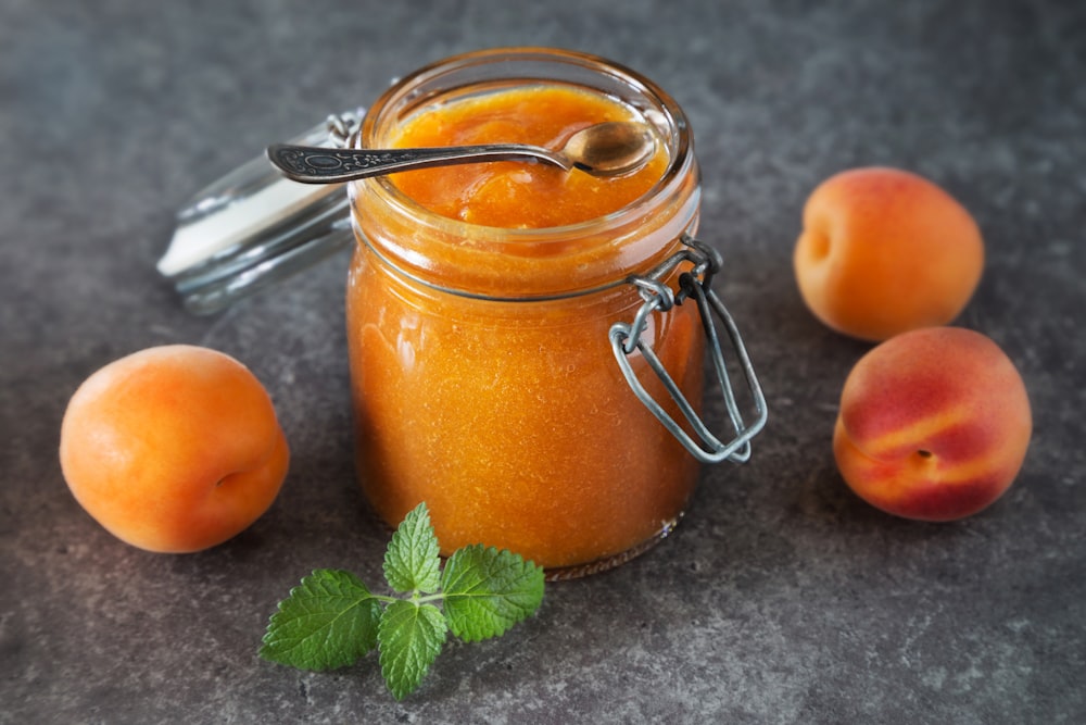 a jar of peach jam next to some peaches