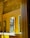 A modern bathroom with bright yellow paneling and mirrors on a textured stone wall. Below the mirrors, there is a white countertop with two sleek faucets and a transparent soap dispenser. A partially visible window allows light to cast shadows across the surfaces.