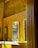A modern bathroom with bright yellow paneling and mirrors on a textured stone wall. Below the mirrors, there is a white countertop with two sleek faucets and a transparent soap dispenser. A partially visible window allows light to cast shadows across the surfaces.