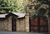 A newly built stone fence with a metal gate surrounded by greenery.