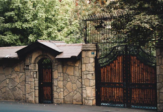 A newly built stone fence with a metal gate surrounded by greenery.