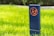 A blue post with an orange sign is placed on a vibrant green lawn. The sign features a crossed-out dog symbol, indicating a restriction on dog walking.