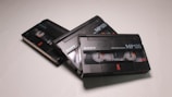 Three black Sony MP120 8mm video cassettes are displayed, positioned diagonally on a light surface. The transparent casing reveals the reels inside, which are partially wound. The brand name and specifications are printed in white text on the front of the cassettes.