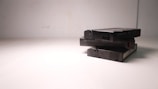 A stack of three VHS tapes placed on a plain, light-colored surface. The tapes are marked with a code and 'Made in Japan' text. The composition is simple, with minimalistic lighting casting soft shadows.