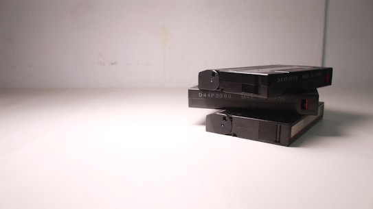 A stack of three VHS tapes placed on a plain, light-colored surface. The tapes are marked with a code and 'Made in Japan' text. The composition is simple, with minimalistic lighting casting soft shadows.