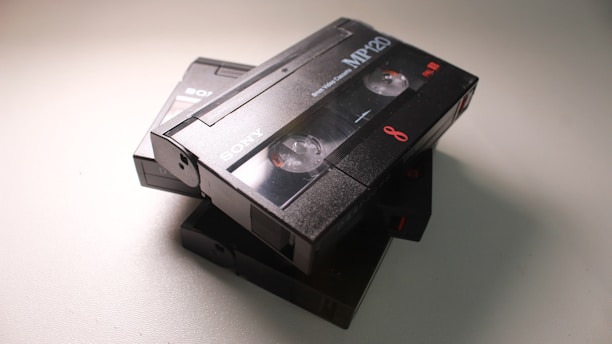A stack of three black Sony camcorder tapes, prominently featuring one labeled MP120, with visible spools and branding. The tapes are slightly overlapping and are shot under soft lighting.