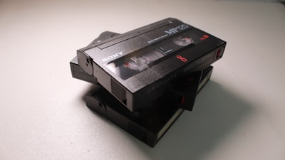 A stack of vintage Sony camcorder tapes, specifically MP120 models, is placed on a light surface. The tapes are black, with visible branding and text indicating 8mm and 'Made in Japan'.