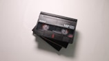 A close-up view of two black video cassette tapes with the label 'Sony MP120' and '8mm Video Cassette' printed on them, placed on a light surface. The tapes are slightly overlapping each other.