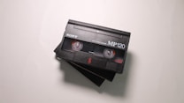 A close-up view of two black video cassette tapes with the label 'Sony MP120' and '8mm Video Cassette' printed on them, placed on a light surface. The tapes are slightly overlapping each other.