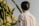 A person with dark hair is wearing a white shirt with a logo on the back and a small Brazilian flag on the sleeve, standing near tall cacti with large white flowers.