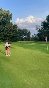 A golfer analyzing putting stats on a smartphone while standing on a green under a bright sunny sky.