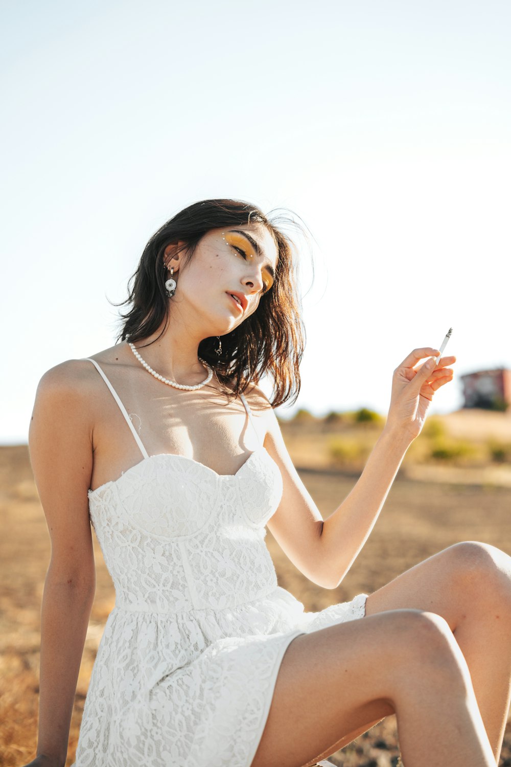 a woman in a white dress holding a cigarette